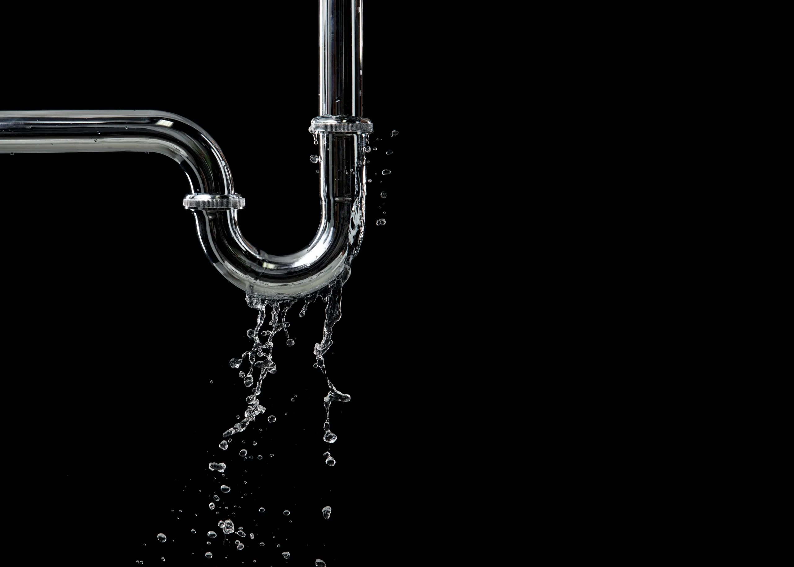 Siphon chromé d'un évier dont les raccords laissent s'échapper de l'eau sur fond noir
